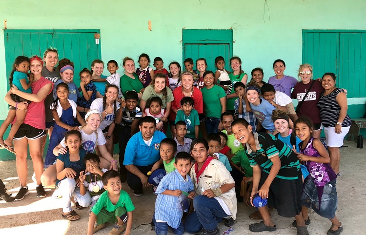 Volleyball team members posing with a group of children from Belize