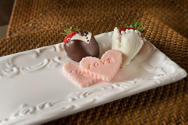 Chocolate covered strawberries and heart shaped candies on a plate